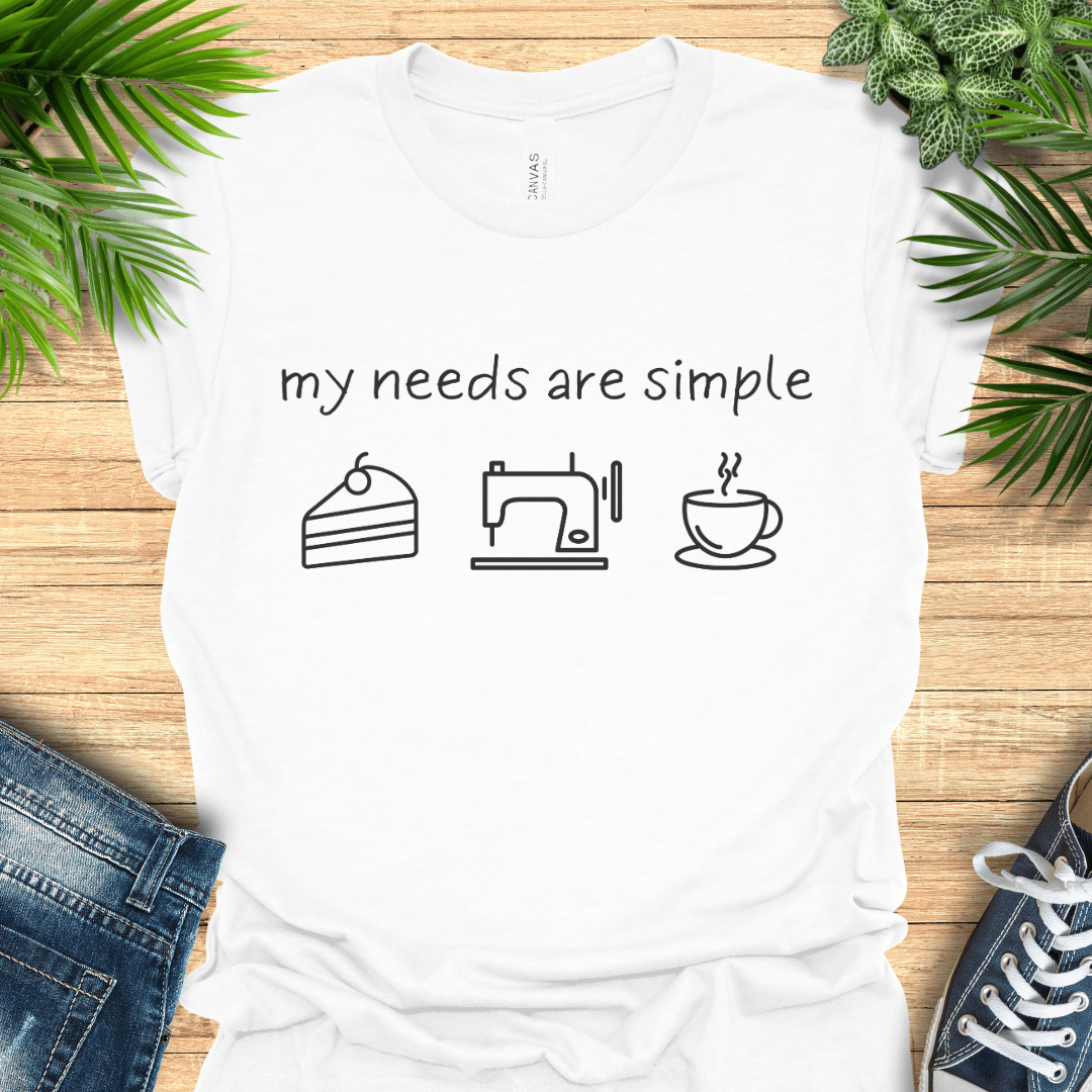 Funny sewing t-shirt with the phrase ‘my needs are simple’ and icons of cake, a sewing machine, and a cup of tea/coffee.