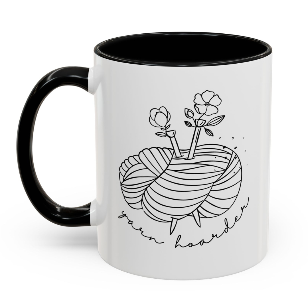 White mug with black interior and handle, featuring a design of yarn and flowers with 'yarn hoarder' text.