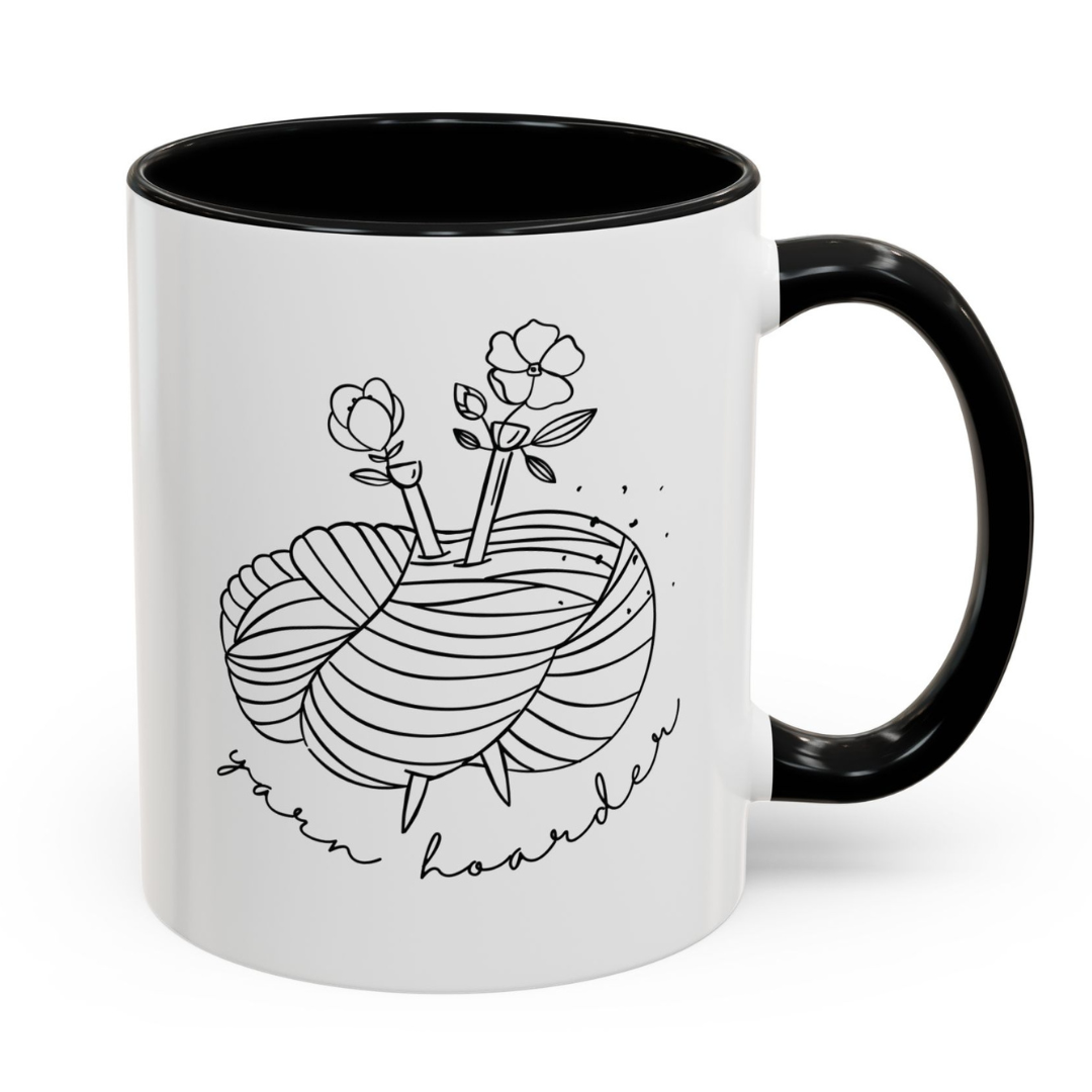 White mug with black interior and handle, featuring a yarn and floral design with 'yarn hoarder' text.