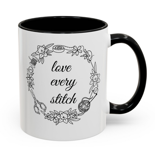 White mug with black interior and handle, featuring a floral wreath and 'love every stitch' text.