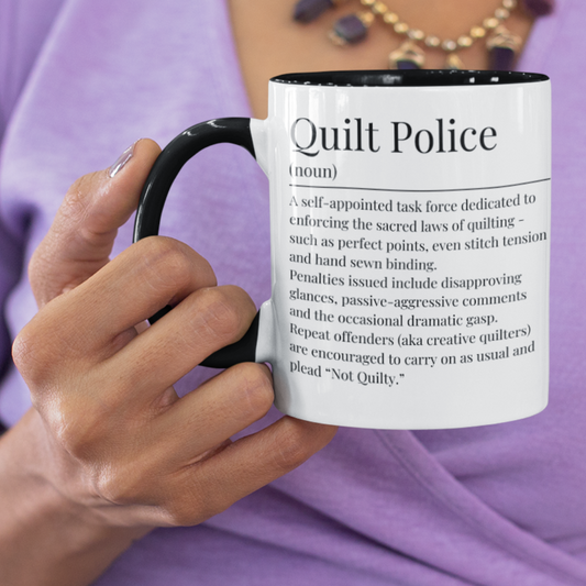 Mug with 'Quilt Police' definition printed on it, held by a person wearing a purple shirt.