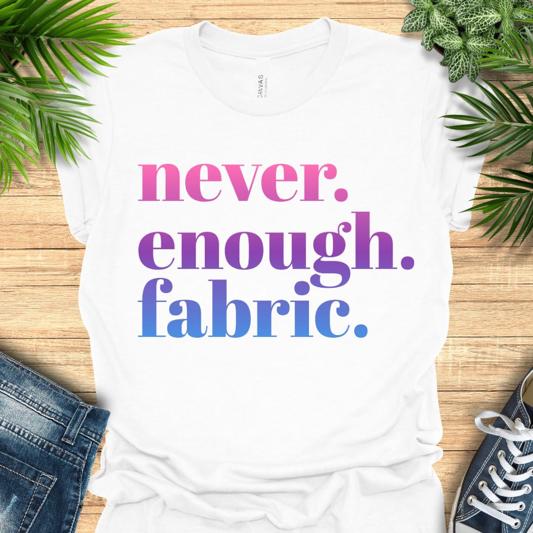Colourful t-shirt for fabric lovers with ‘never. enough. fabric.’ in pink-to-blue gradient text. Ideal for sewing enthusiasts.