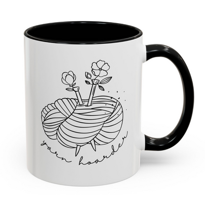 White mug with black interior and handle, featuring a yarn and floral design with 'yarn hoarder' text.